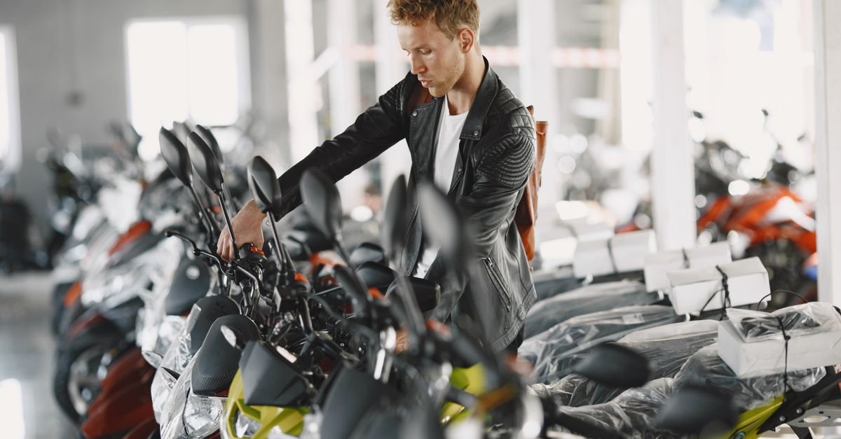 Homem observa fileira de motocicletas novas em showroom de concessionária