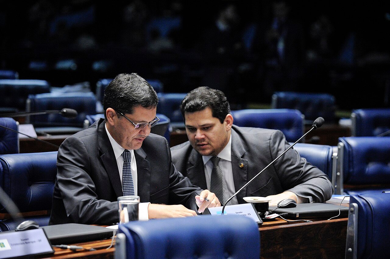 Senador Davi Alcolumbre sentado na bancada do plenario do Senado ao lado de outro parlamentar