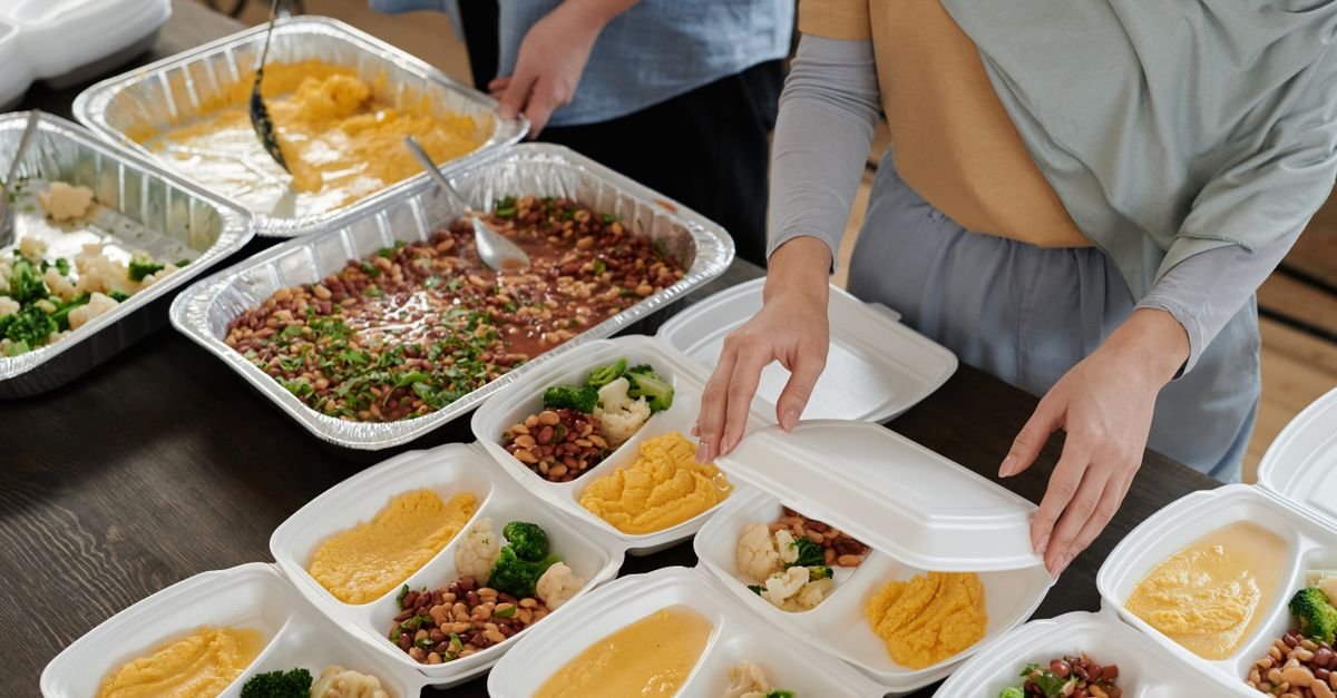 Marmitas sendo montadas com arroz, feijão e legumes sobre uma mesa