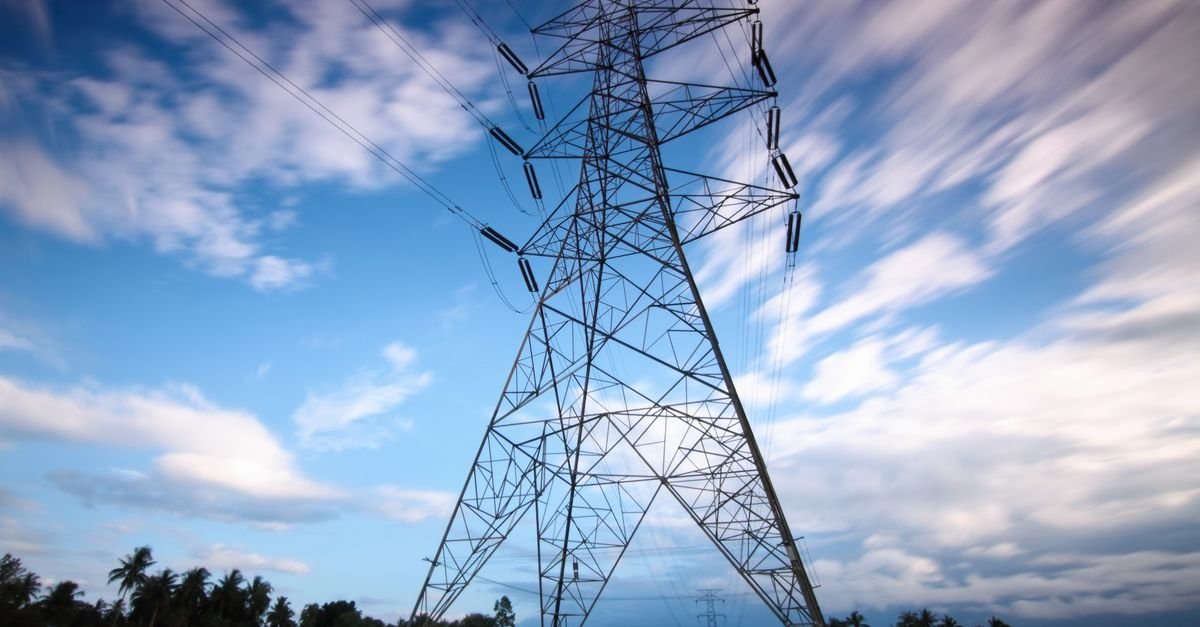 Torre de transmissão de energia de alta tensão vista de baixo contra o céu com nuvens