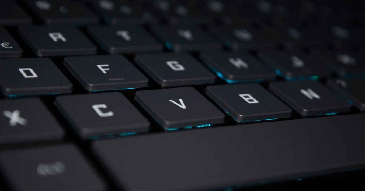 Teclado de computador preto com iluminação azul em ambiente escuro