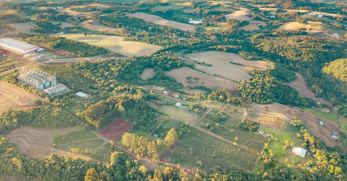 Vista aérea de área rural no Sul do Brasil, com lavouras, mata, silos e propriedades