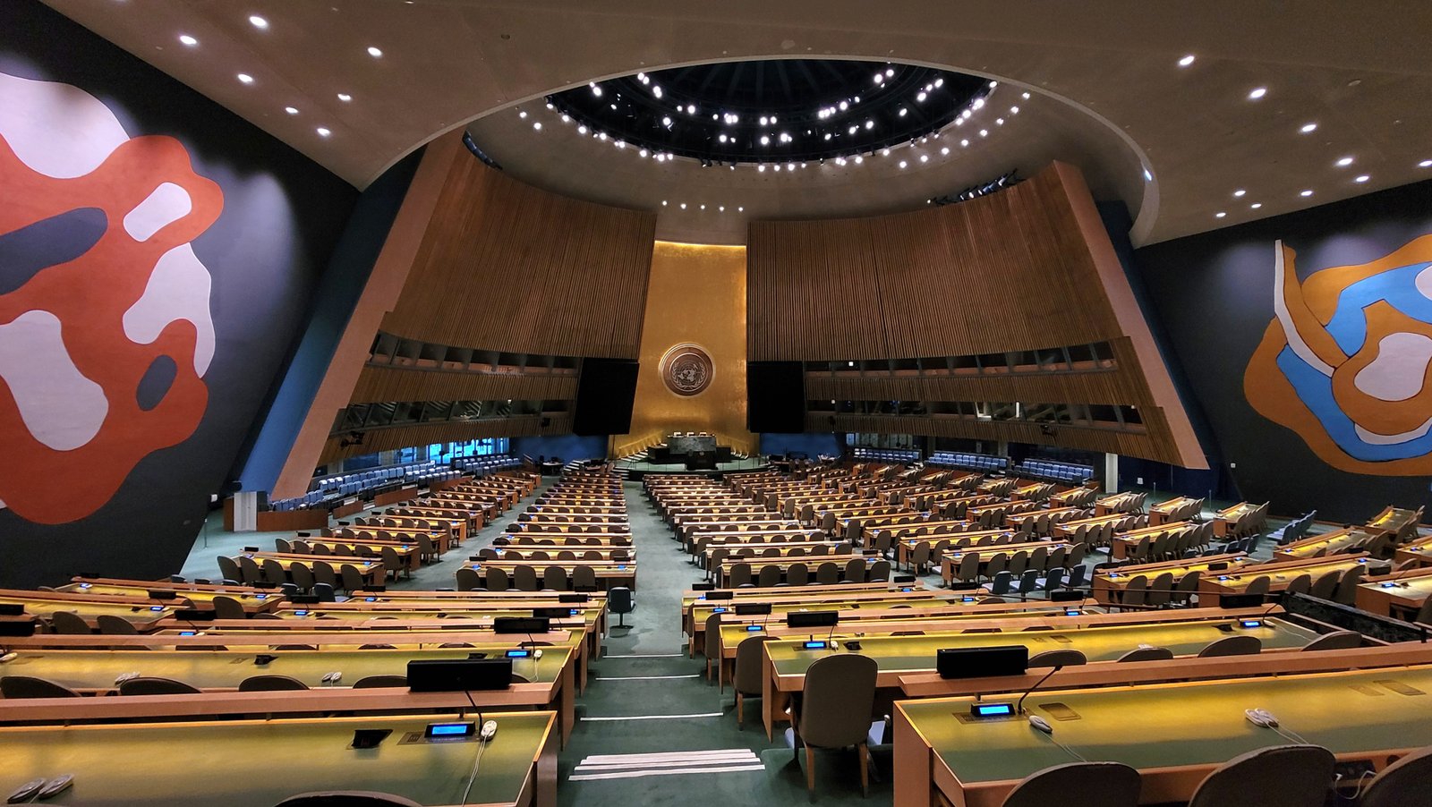Plenário da Assembleia Geral da ONU, na sede da organização em Nova York, com as bancadas vazias e o emblema dourado ao fundo
