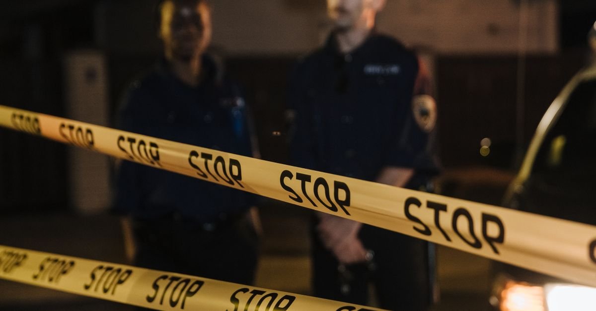 Fita de isolamento policial estendida à frente de dois agentes durante atendimento de ocorrência