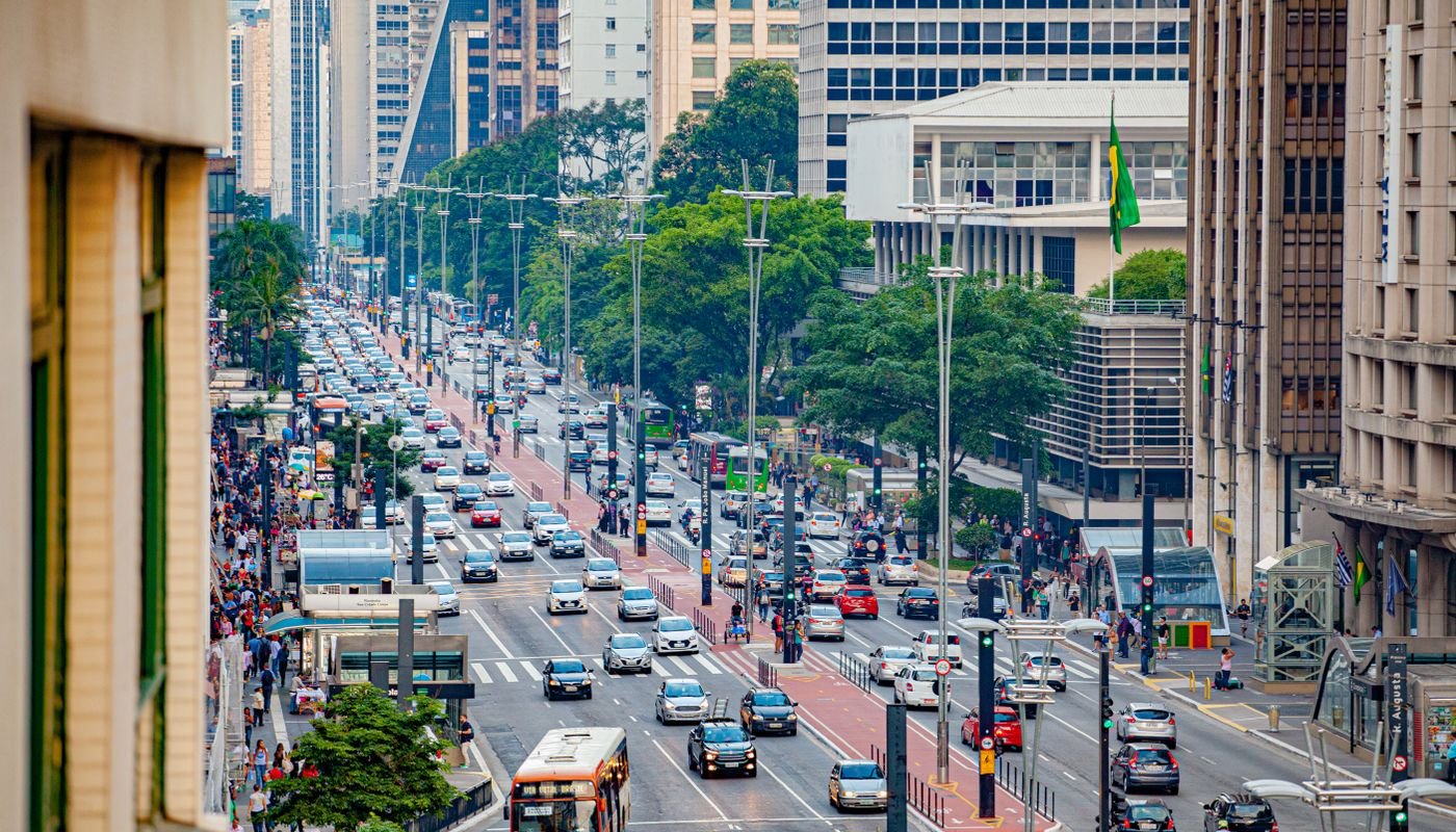 Vista aérea da Avenida Paulista, em São Paulo, com trânsito intenso, pedestres nas calçadas e bandeira do Brasil hasteada
