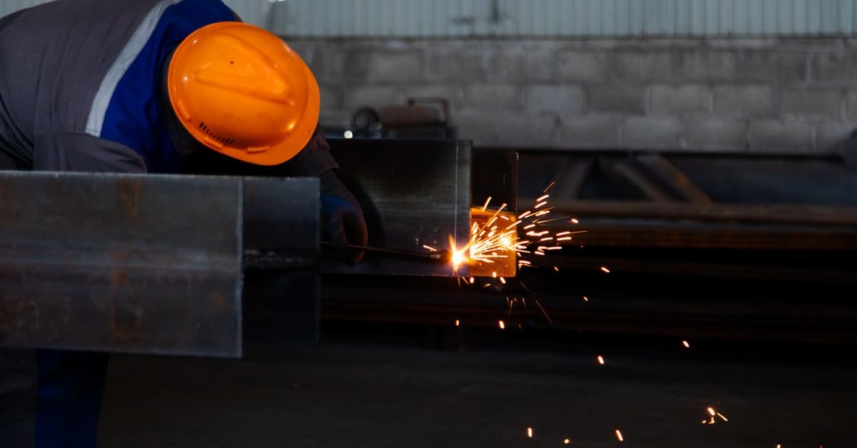 Operário com capacete de segurança solda estrutura metálica em galpão industrial