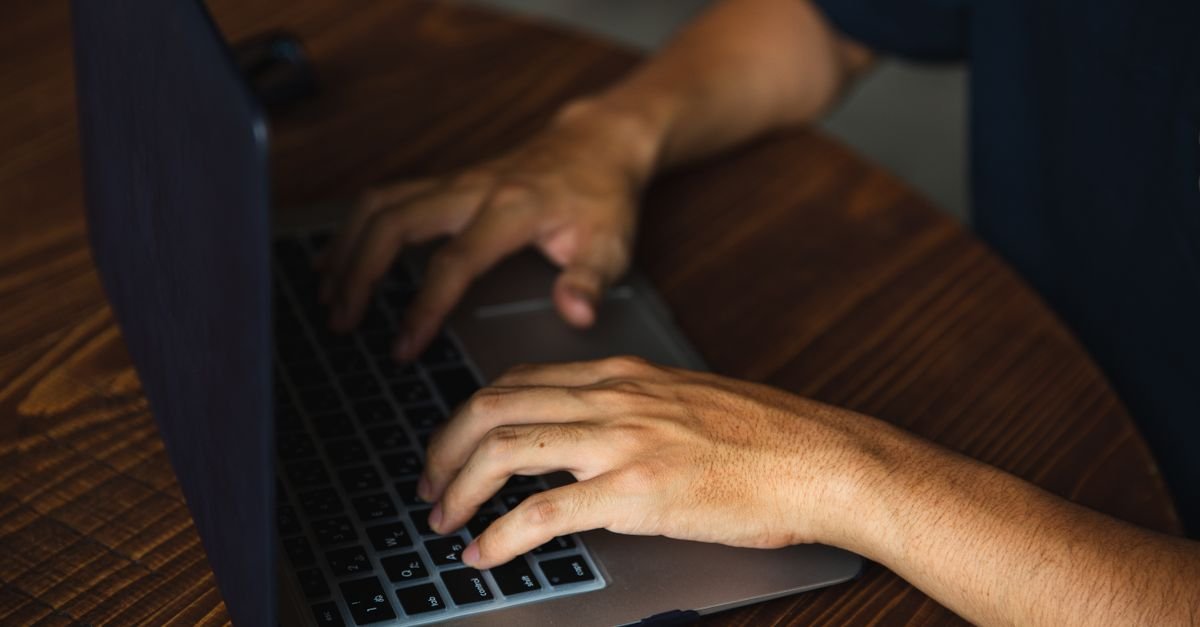 Mãos digitam no teclado de um notebook sobre mesa de madeira