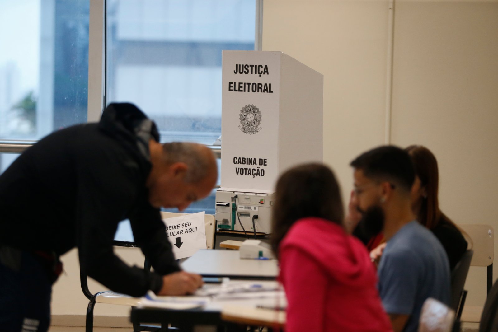 Cabina de votação da Justiça Eleitoral com urna eletrônica e mesários em seção