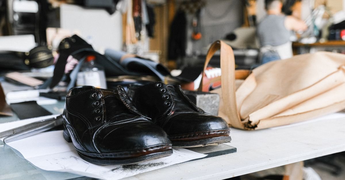 Par de sapatos de couro preto sobre bancada de oficina de calcados, com ferramentas ao fundo