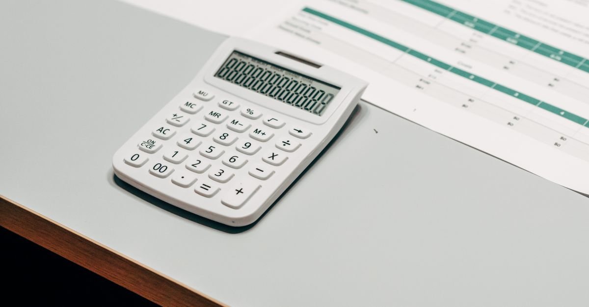Calculadora branca sobre mesa clara ao lado de uma planilha financeira impressa