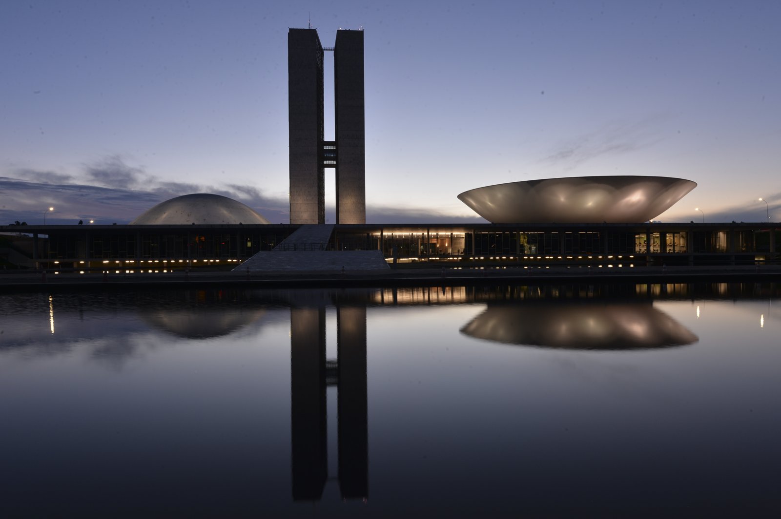 Palácio do Congresso Nacional ao anoitecer, com as torres, a cúpula do Senado e a da Câmara refletidas no espelho d'água