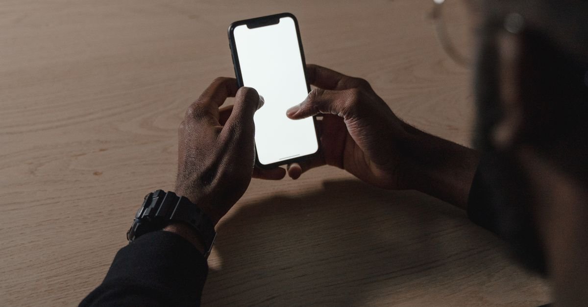 Mãos seguram celular com a tela acesa sobre mesa de madeira