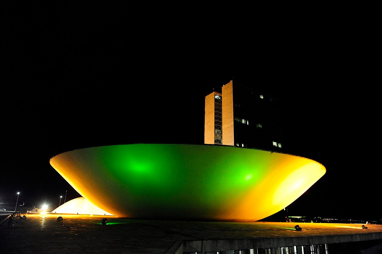 Congresso Nacional iluminado em verde e amarelo à noite, com as torres ao fundo
