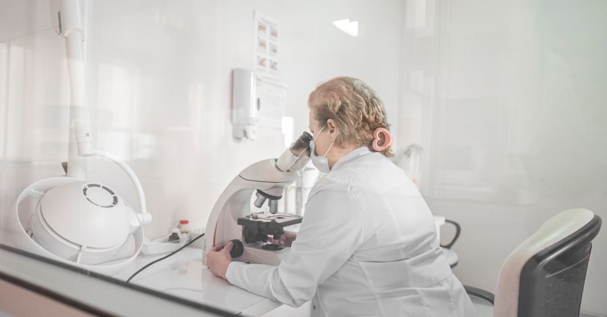 Cientista de jaleco branco trabalha com microscópio em laboratório