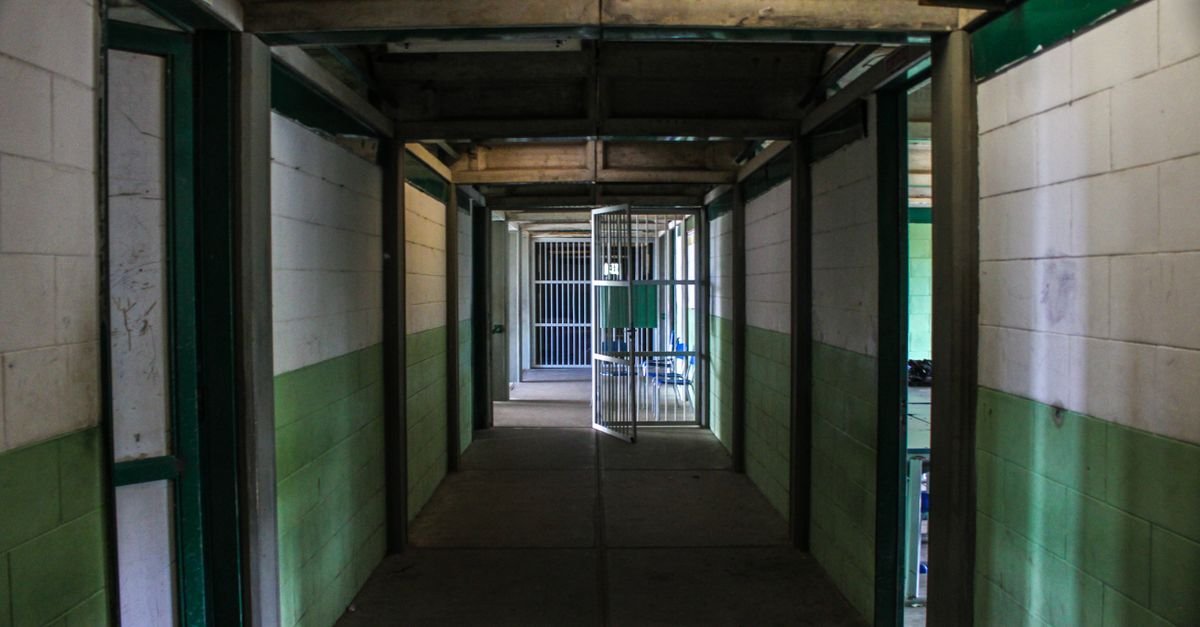 Corredor de unidade prisional com grade aberta ao fundo e paredes pintadas em verde e branco