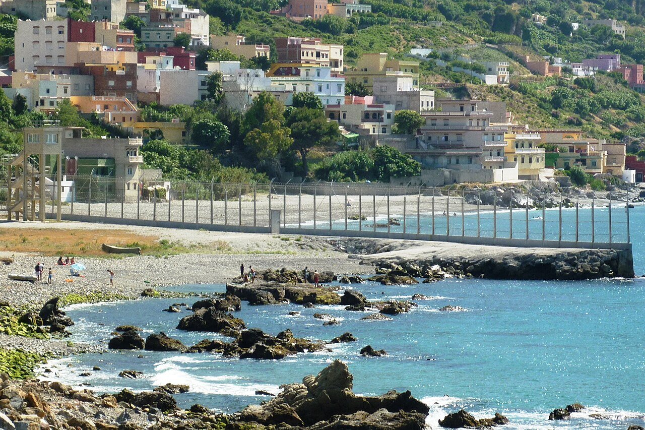 Cerca que marca a fronteira entre Ceuta e o Marrocos, com o mar e casas ao fundo