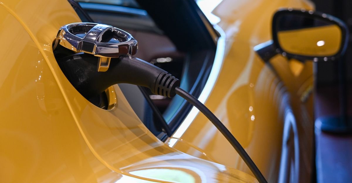 Cabo de recarga plugado na tomada de um carro elétrico amarelo, em primeiro plano