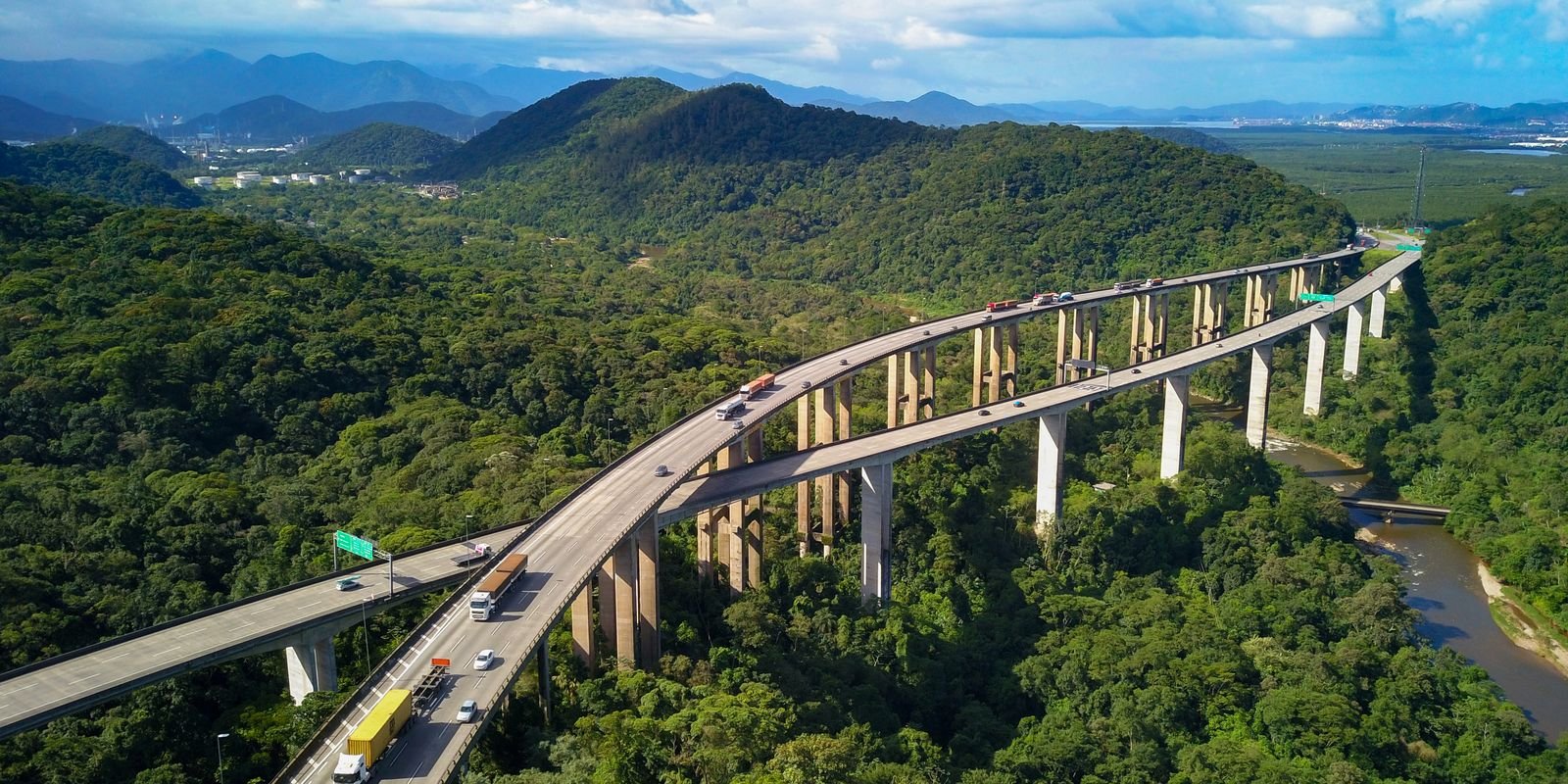 Vista aerea de rodovia elevada com caminhoes cruzando area de mata