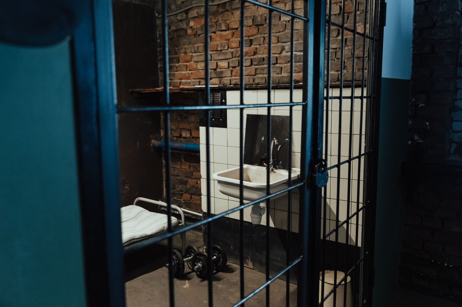 Cela vazia com porta de grade aberta, cama de ferro e pia
