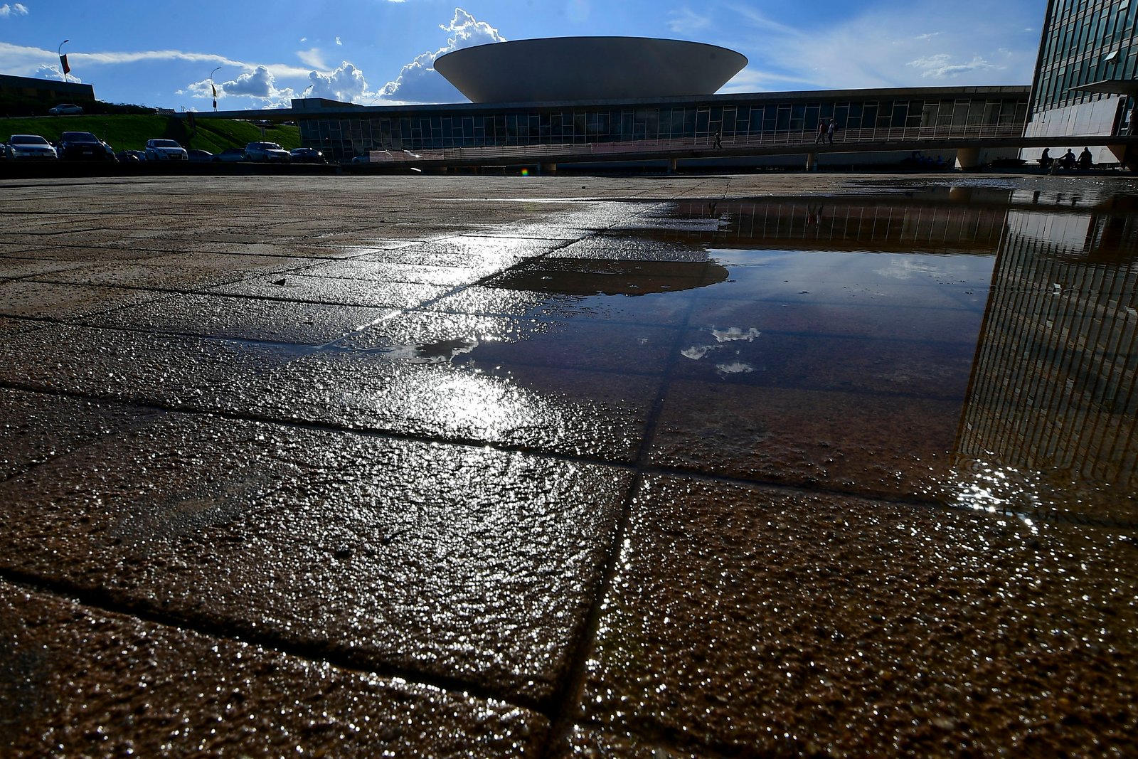 Fachada do Congresso Nacional refletida em poças de água na esplanada, em Brasília