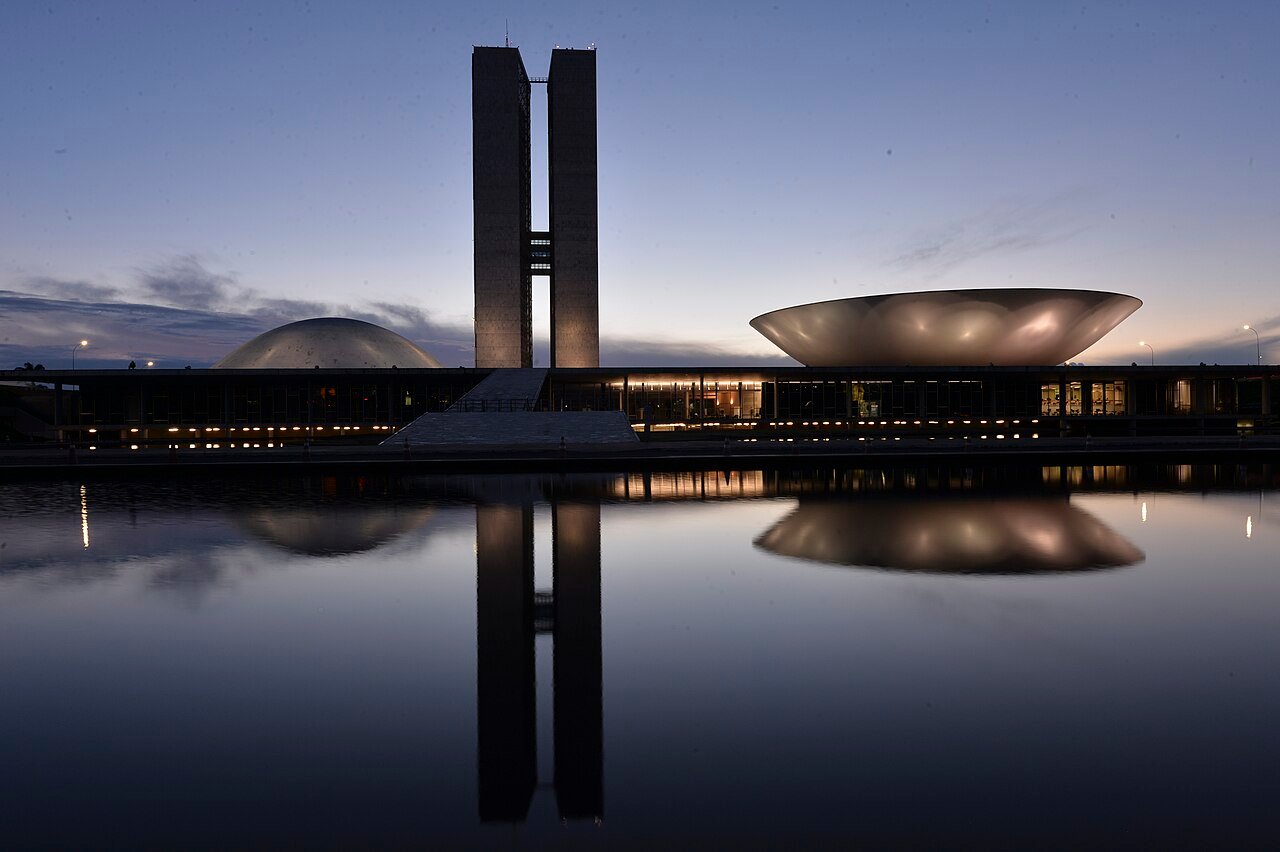 Prédio do Congresso Nacional refletido no espelho d'água ao entardecer, em Brasília