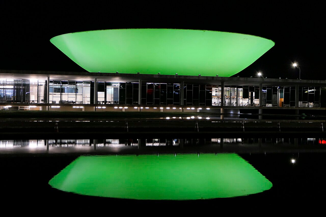 Cúpula do Senado no Congresso Nacional iluminada à noite, refletida no espelho d'água