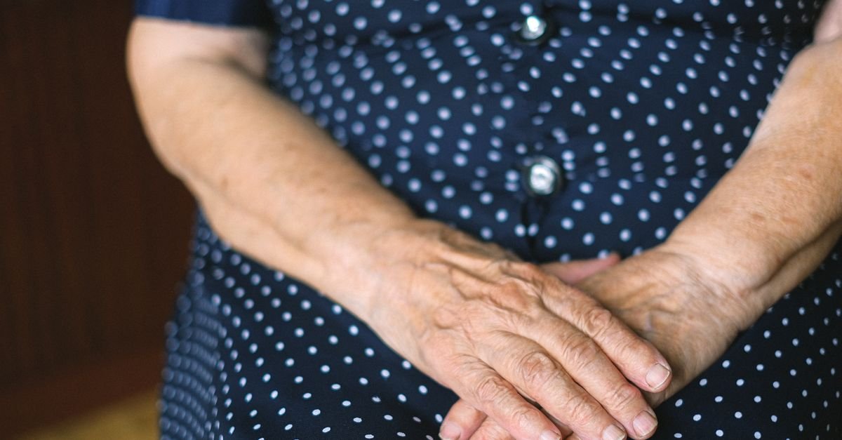 Maos de uma pessoa idosa cruzadas sobre um vestido azul de bolinhas brancas