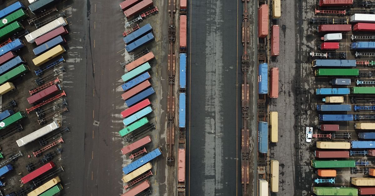 Vista aérea de pátio com contêineres de carga alinhados em terminal logístico