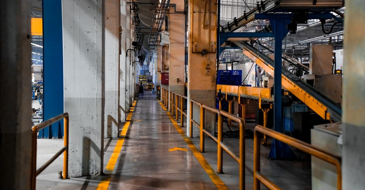 Corredor de fábrica vazio, com corrimãos amarelos, esteiras e maquinário parado