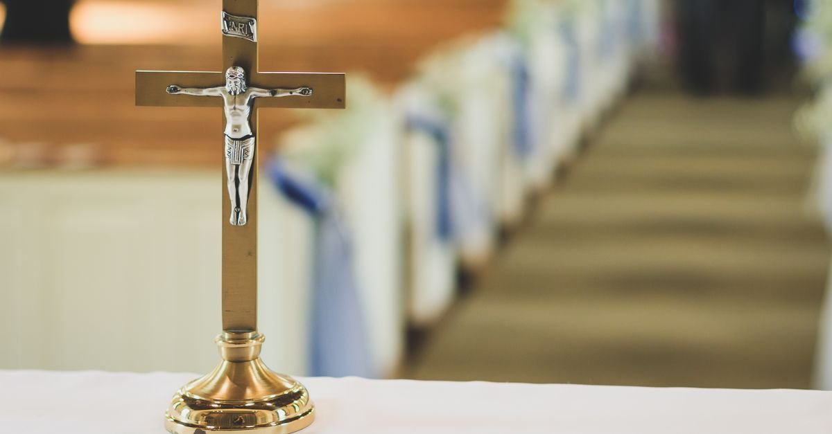 Crucifixo dourado sobre o altar de uma igreja católica, com os bancos ao fundo desfocados