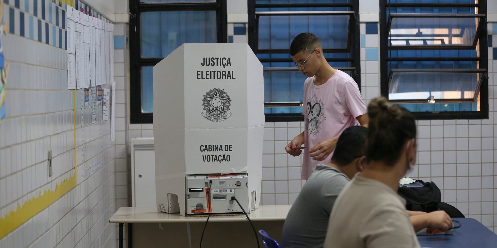 Eleitor diante de cabina de votação da Justiça Eleitoral com urna eletrônica