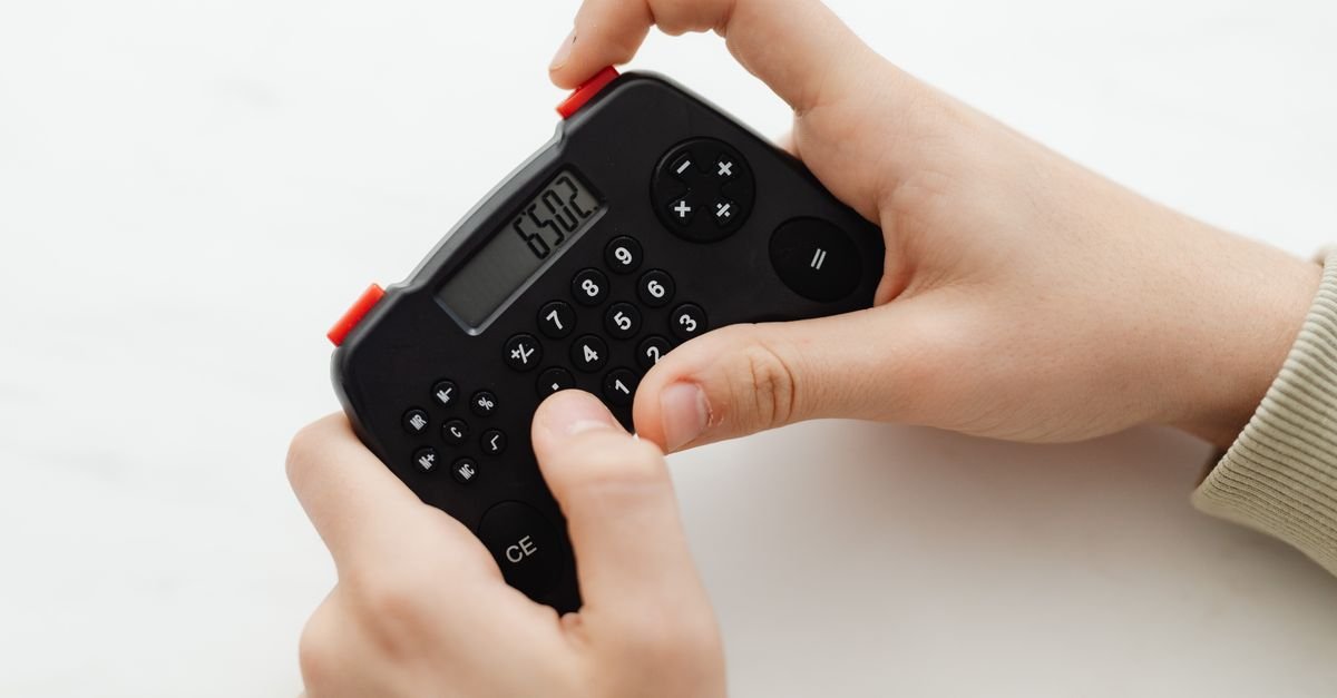 Mãos operando calculadora preta sobre mesa branca