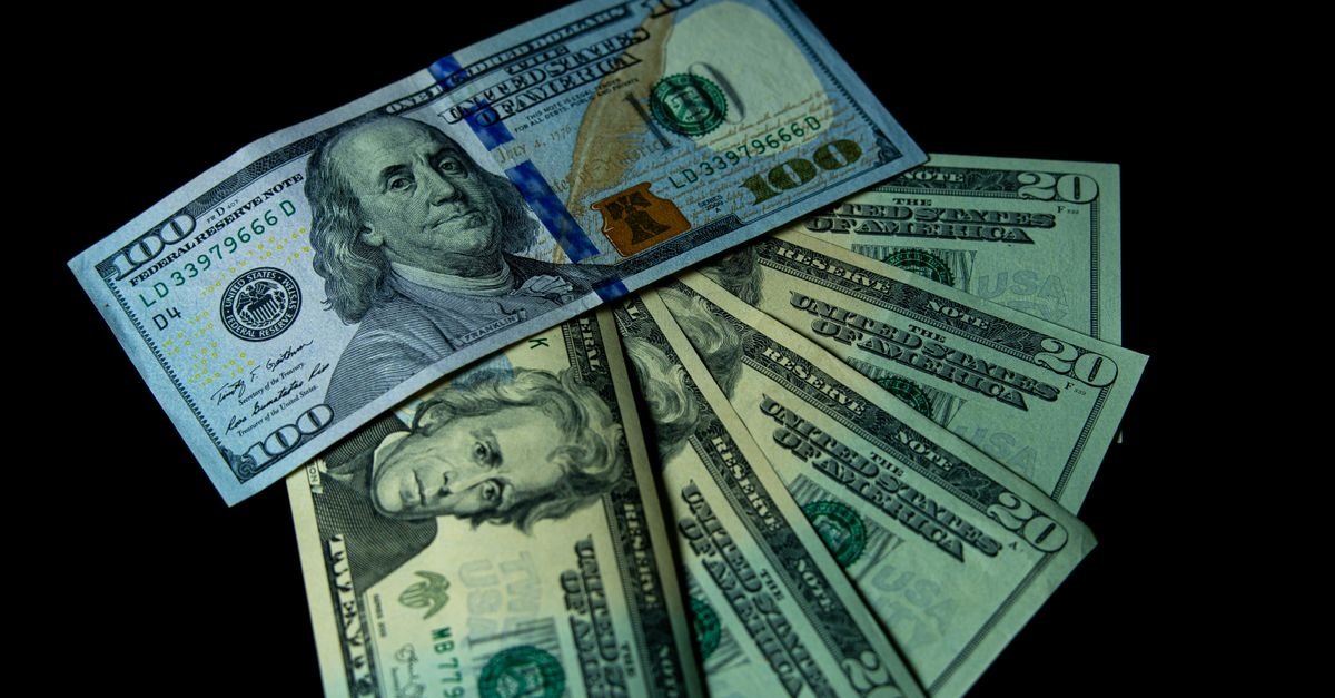 Cédulas de dólar americano de 100 e 20 dólares dispostas sobre fundo escuro