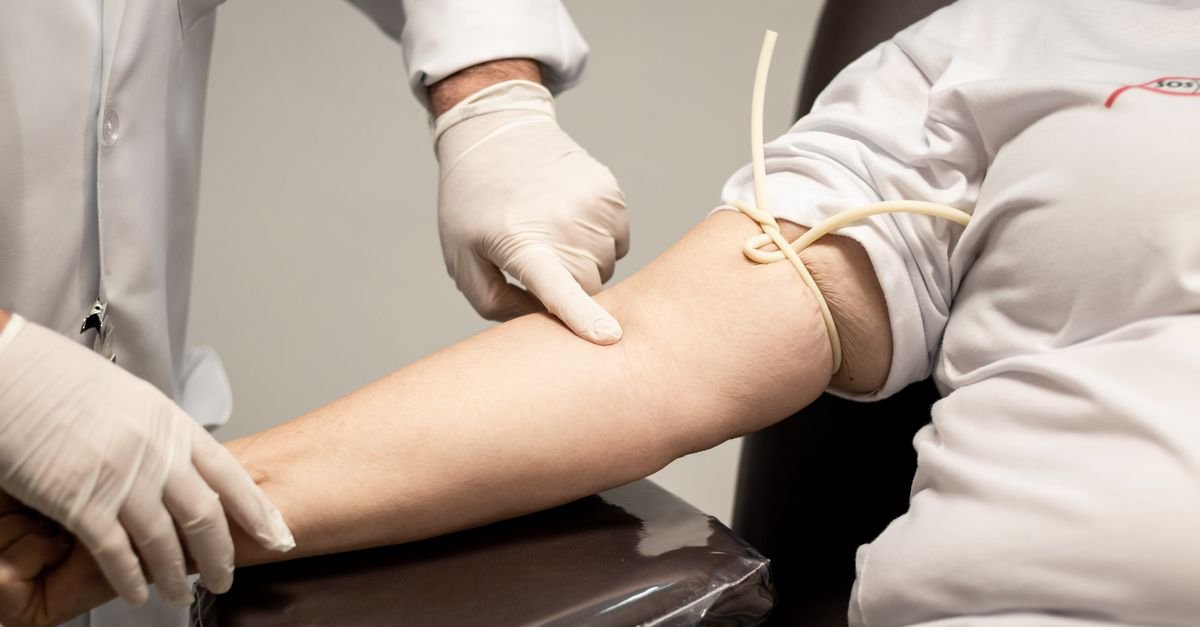 Profissional de saúde com luvas prepara o braço de um doador com garrote antes da coleta de sangue