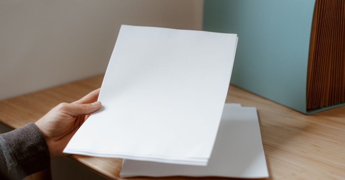 Mão segura folhas de papel sobre mesa de madeira com pasta de documentos