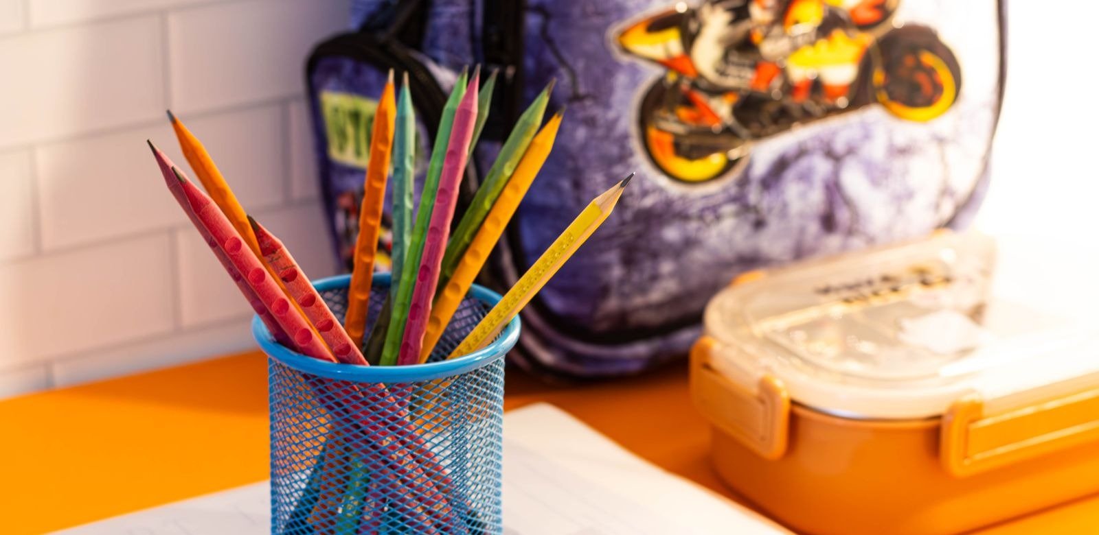 Copo de lápis coloridos sobre cadernos e mochila escolar em uma mesa