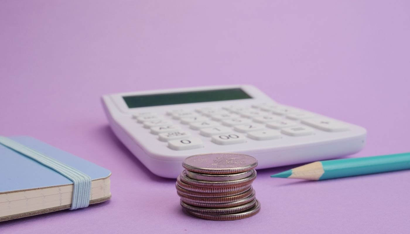 Calculadora, pilha de moedas, caderno e lápis sobre superfície lisa
