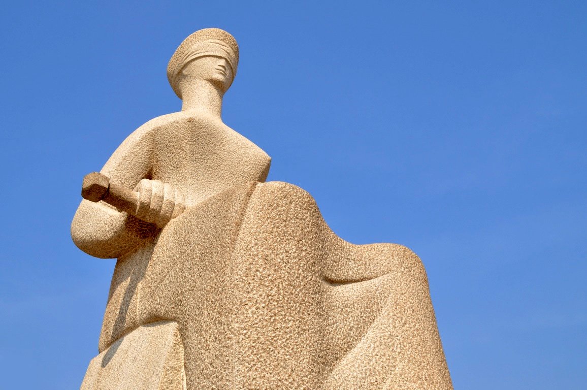 Estátua da Justiça, escultura de mulher vendada com espada, contra o céu azul