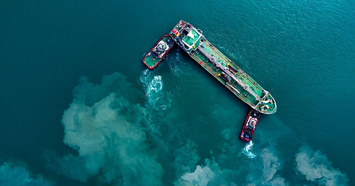 Vista aerea de petroleiro rebocado por duas embarcacoes em mar aberto de agua turquesa