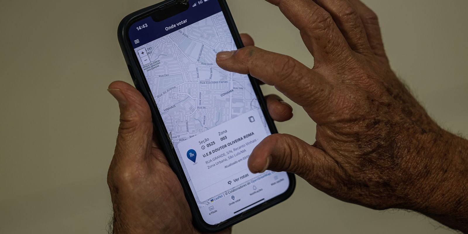 Mãos de eleitor seguram celular com a tela onde votar do aplicativo e-Título
