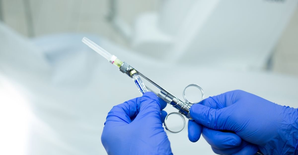 Mãos com luvas cirúrgicas seguram seringa com agulha em ambiente clínico