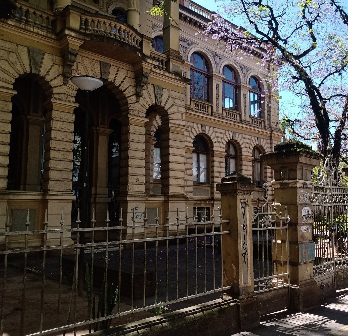Fachada histórica do prédio da Faculdade de Direito da UFRGS, em Porto Alegre, com grade e árvores floridas