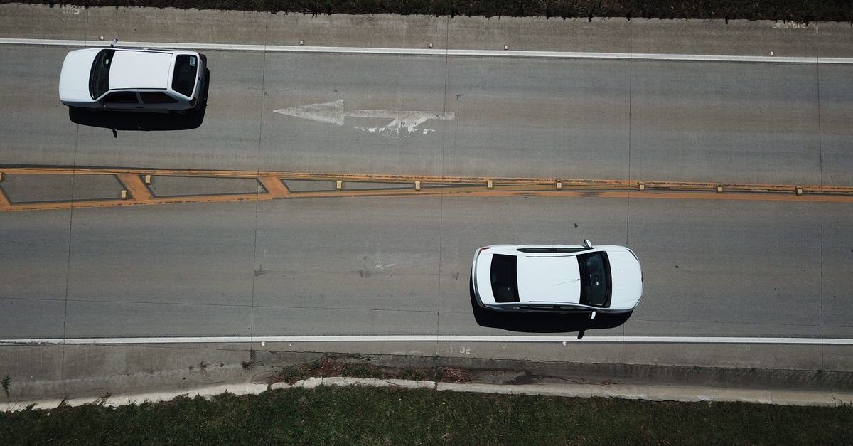 Vista aérea de dois carros em uma rodovia de pista dupla com faixas de sinalização