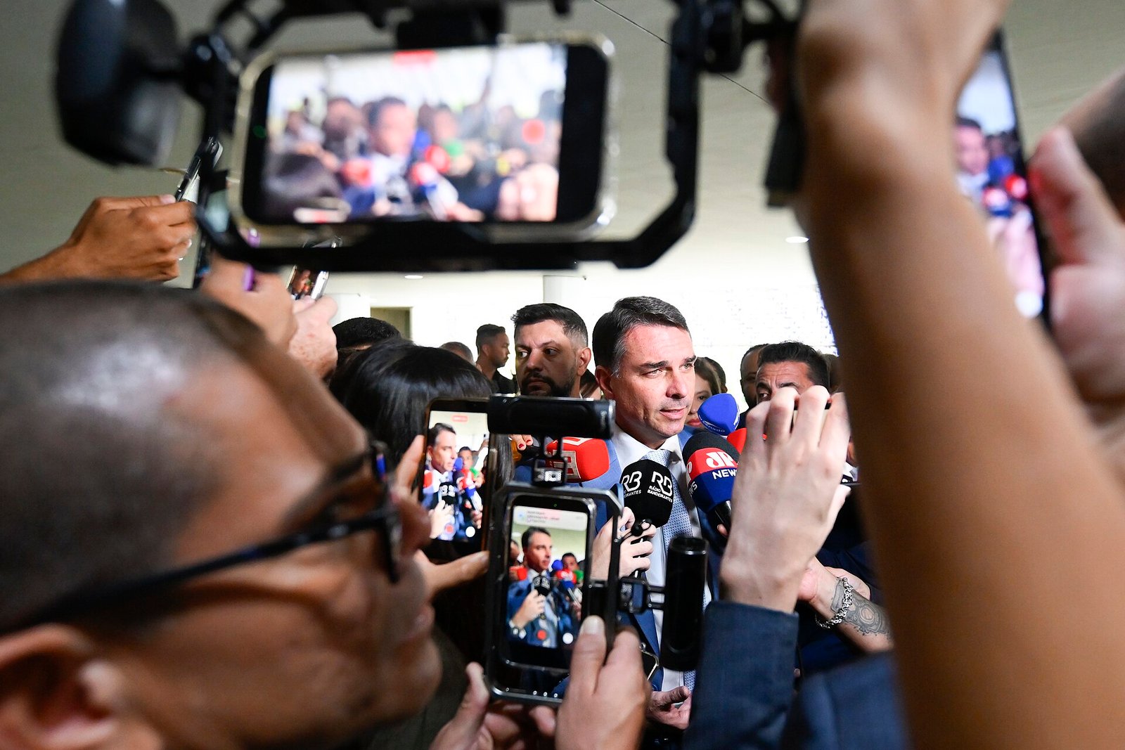 Senador Flávio Bolsonaro fala a jornalistas cercado por microfones e celulares durante entrevista coletiva