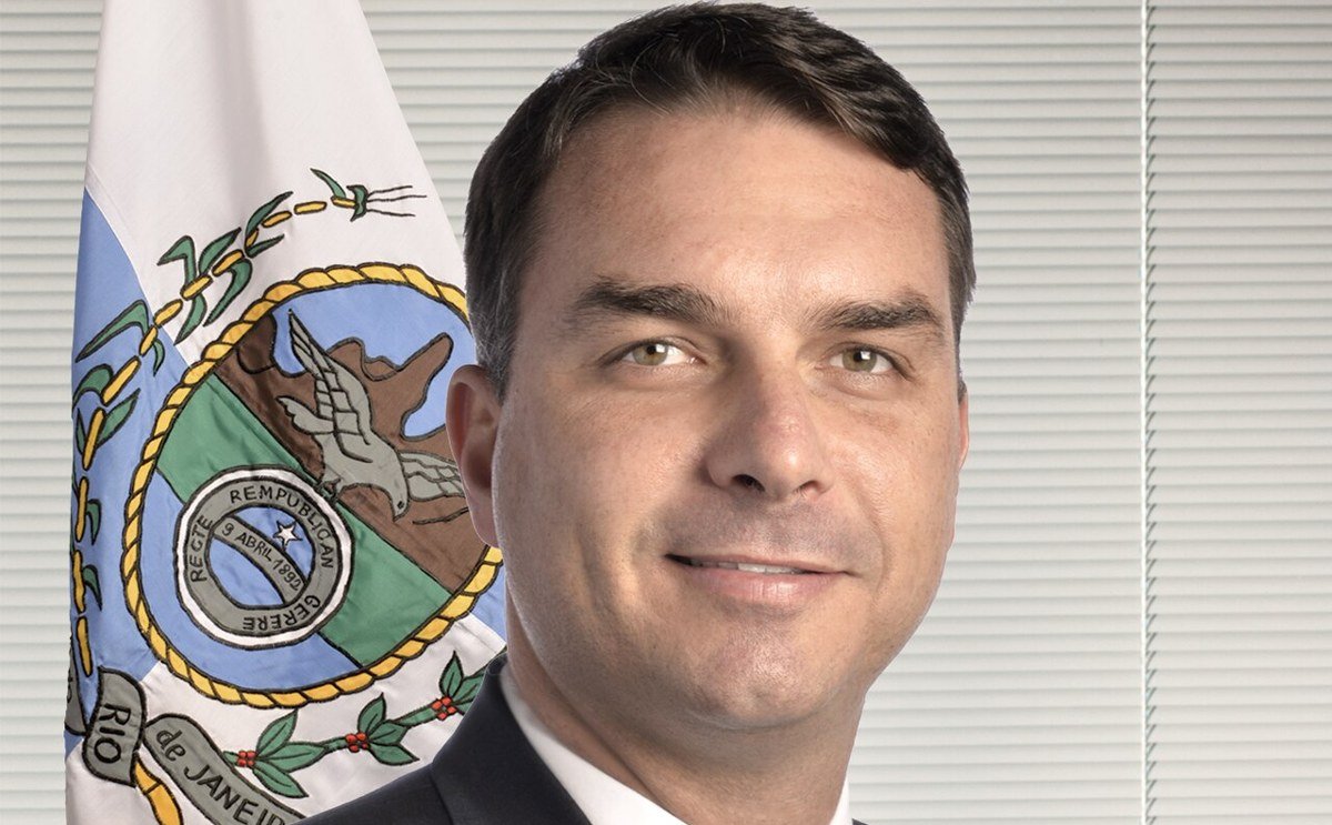 Foto oficial do senador Flávio Bolsonaro ao lado da bandeira do Rio de Janeiro