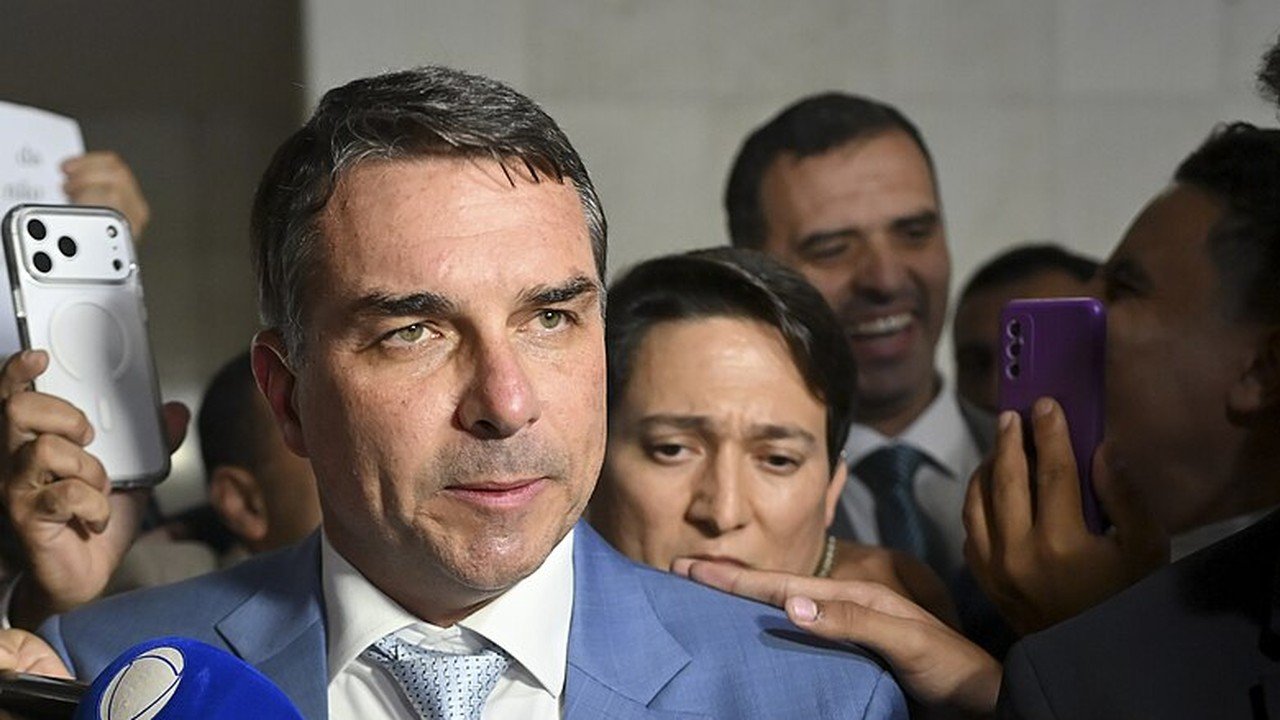 O senador Flávio Bolsonaro fala a jornalistas cercado por microfones e celulares em corredor do Senado
