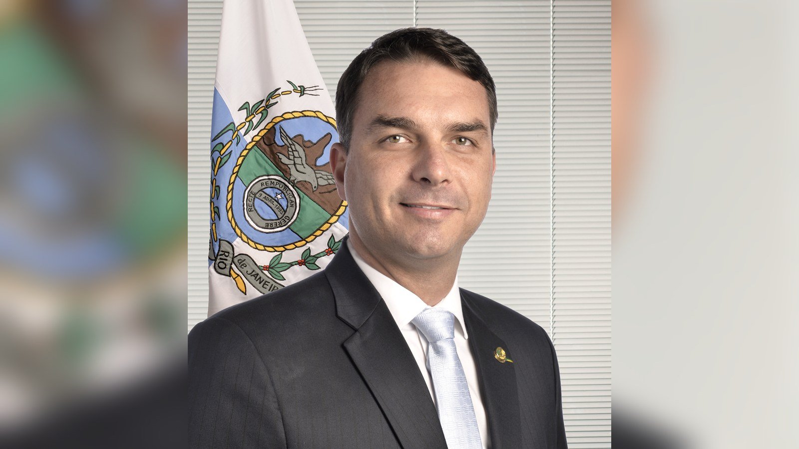 Retrato oficial do senador Flávio Bolsonaro ao lado da bandeira do Rio de Janeiro