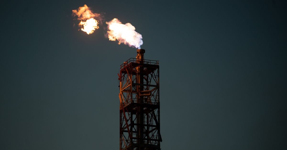 Chaminé industrial com queima de gás em chama contra céu escuro