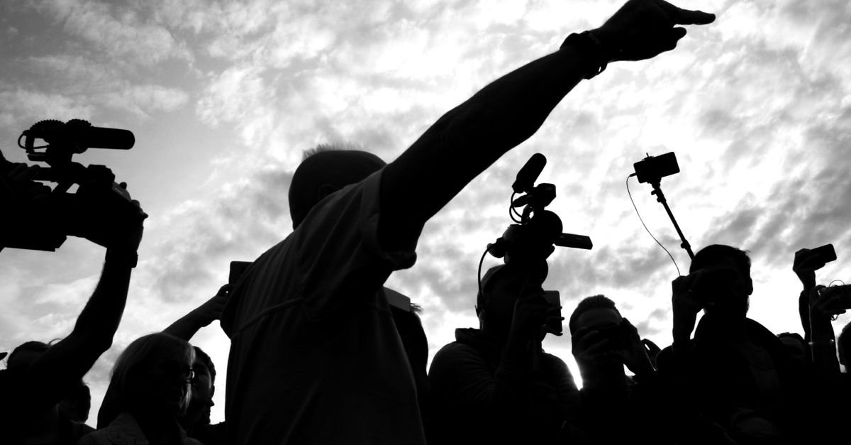 Silhuetas de profissionais de imprensa com câmeras e microfones erguidos contra o céu nublado
