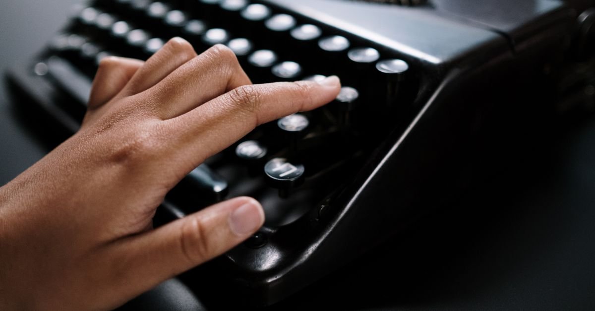 Mao digitando em maquina de escrever antiga sobre mesa escura
